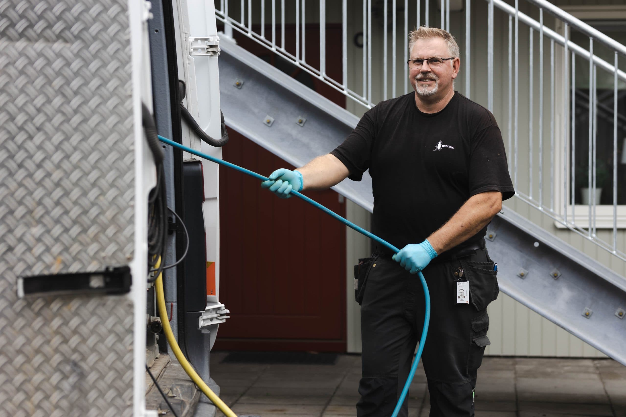 Spoltec användare i handskar slangar nära en metalltrappa och byggnad.