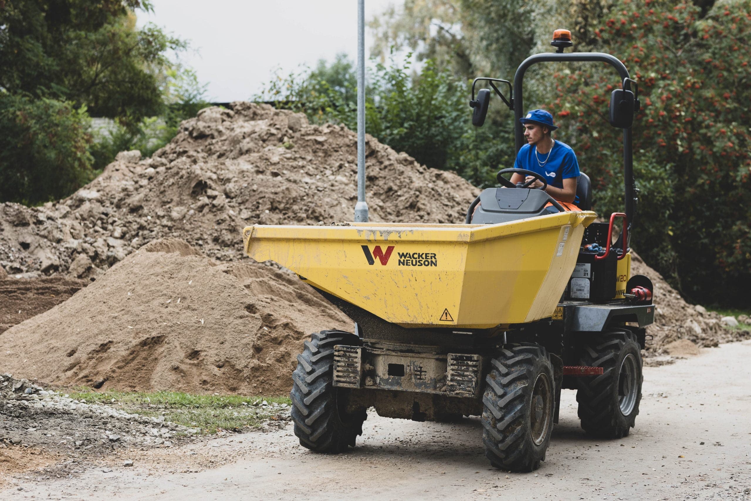 Person som kör en gul Wacker Neuson dumper nära en hög med smuts på en Spoltec-byggarbetsplats.
